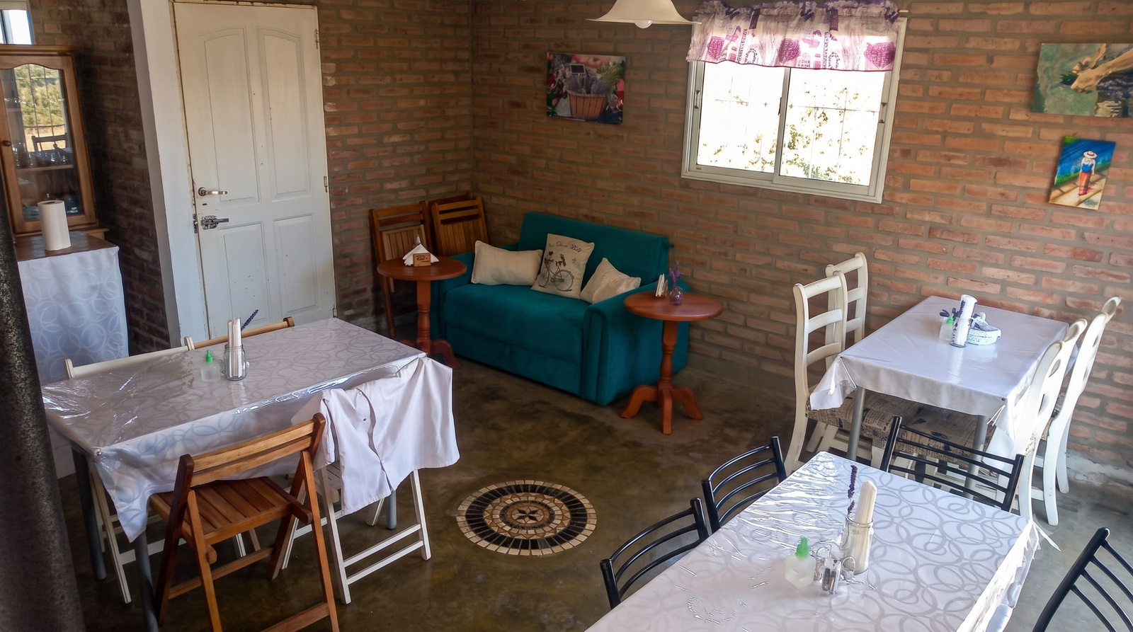 Salón interior de MAMU Casa de Té — mesas, sillas de madera, sofá turquesa y cuadros en pared de ladrillo