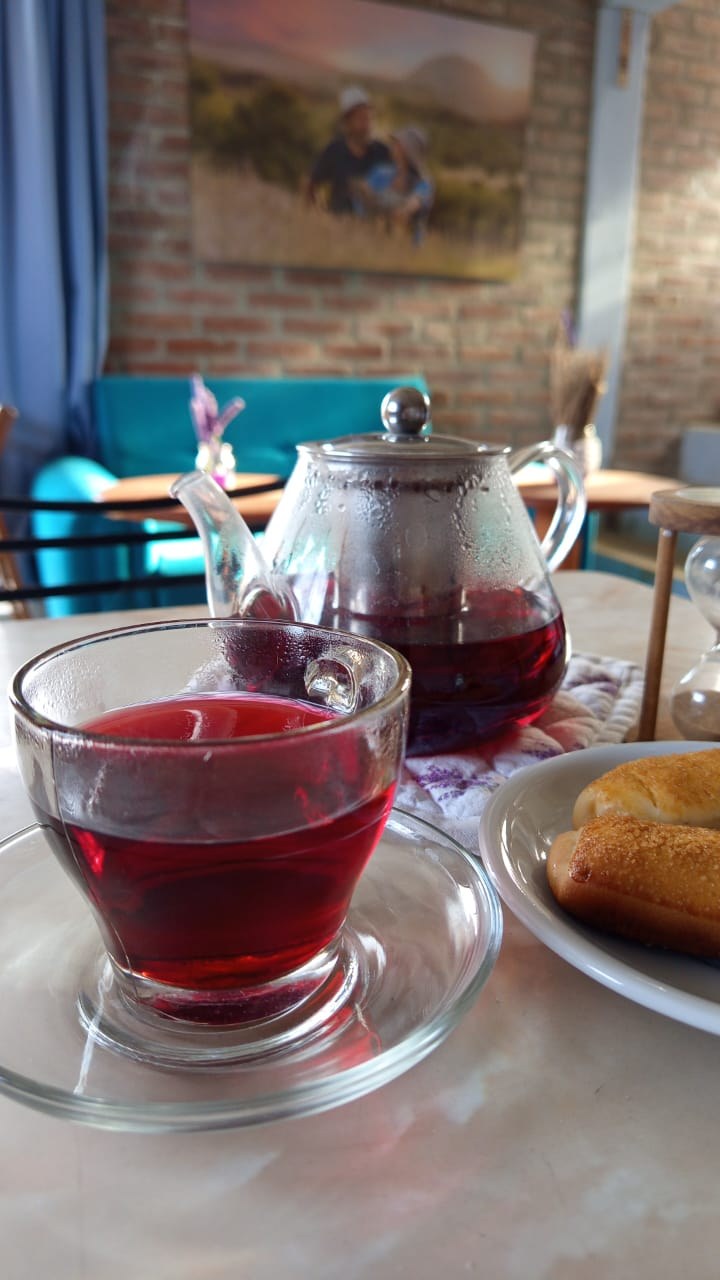 Tetera de vidrio con té rojo servido en taza, con panecillos artesanales — infusión de la casa en MAMU Calmayo